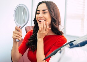 Woman smiling at reflection in handheld mirror