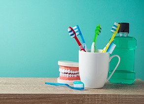 A cup holding multiple toothbrushes while a mouth mold and bottle of mouthwash all sit on a table