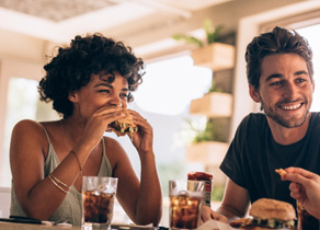 Woman eating burger while sitting next to man in restaurant
