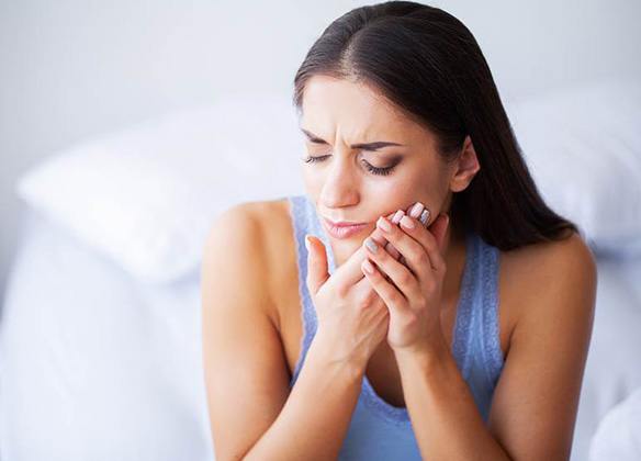 Woman sitting on bed with tooth pain
