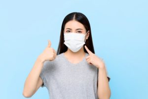 young woman wearing face mask and giving thumbs up