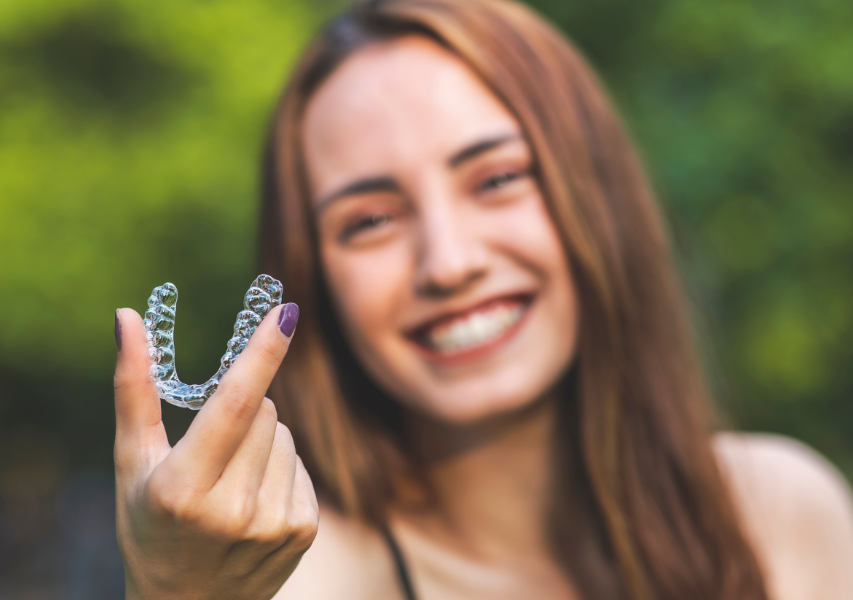 Woman smiling, holding clear aligner